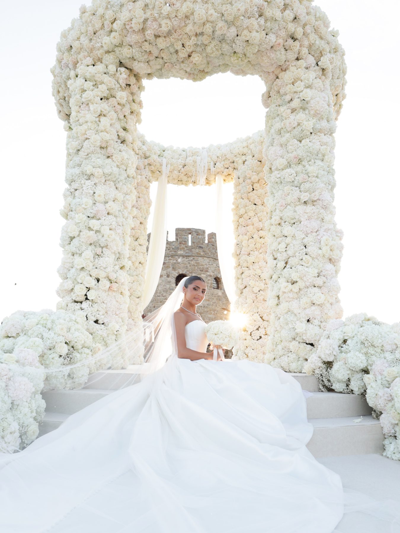 Bride in sleek low bun portrait framed by floral arch, Castello di Rocca Cilento, Italy