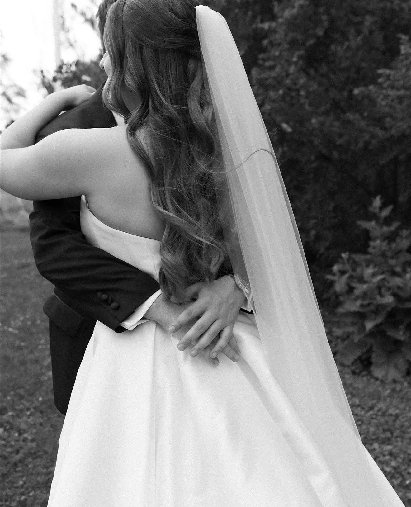 Close-up of bride's half-up curls with veil, embracing groom, black and white