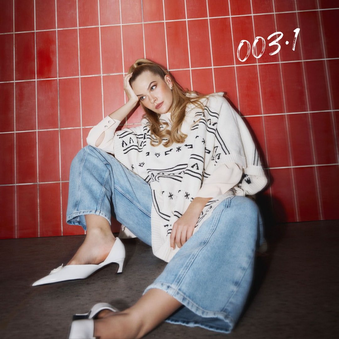 Model with loose waves seated against red tile backdrop, campaign photoshoot
